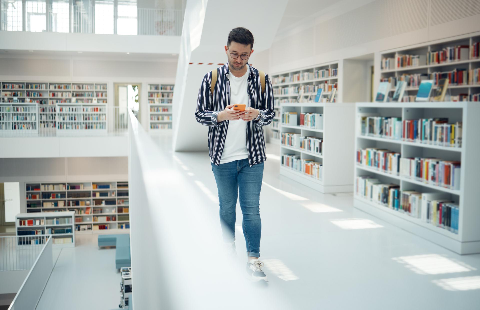 Student walking in library with phone for university, education or college website, internet search and academy faq, about us or contact. Campus, cellphone and teenager reading scholarship newsletter